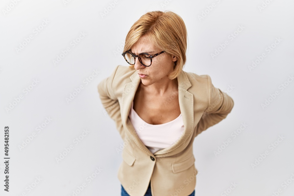 Middle age blonde business woman standing over isolated background suffering of backache, touching back with hand, muscular pain Middle age blonde business woman standing over isolated background suffering of backache, touching back with hand, muscular pain