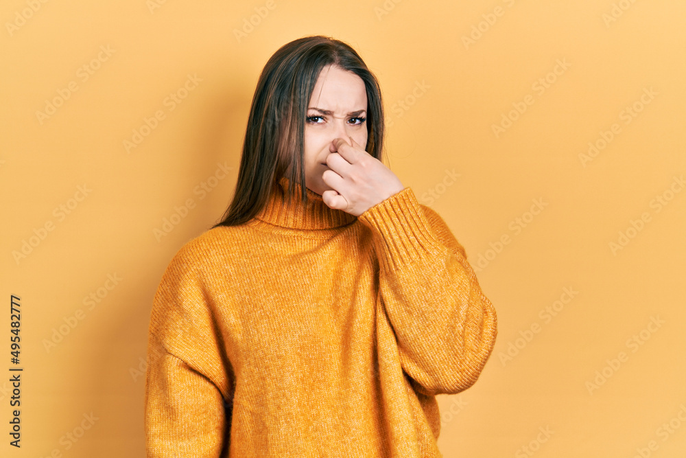 Young hispanic girl wearing casual clothes smelling something stinky and disgusting, intolerable smell, holding breath with fingers on nose. bad smell Young hispanic girl wearing casual clothes smelling something stinky and disgusting, intolerable smell, holding breath with fingers on nose. bad smell