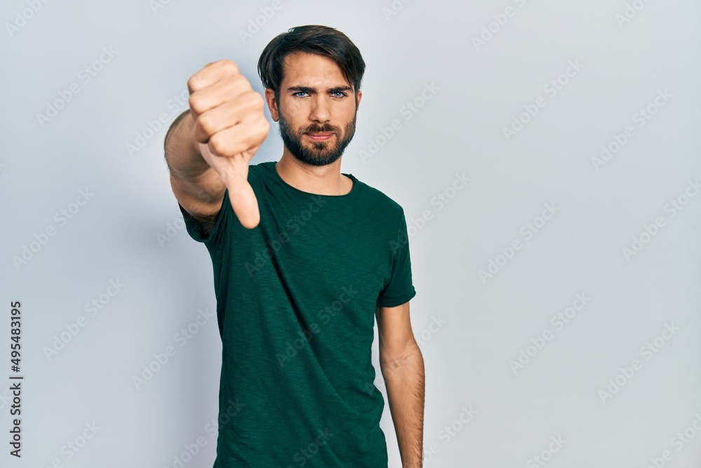 Fototapeta premium Young hispanic man wearing casual white tshirt looking unhappy and angry showing rejection and negative with thumbs down gesture. bad expression.