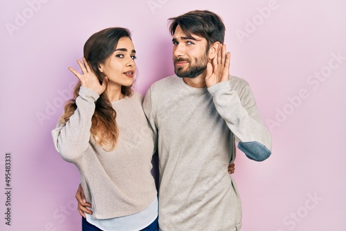 Young hispanic couple wearing casual clothes smiling with hand over ear listening an hearing to rumor or gossip. deafness concept.