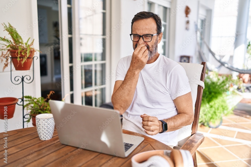 Middle age man using computer laptop at home smelling something stinky and disgusting, intolerable smell, holding breath with fingers on nose. bad smell Middle age man using computer laptop at home smelling something stinky and disgusting, intolerable smell, holding breath with fingers on nose. bad smell