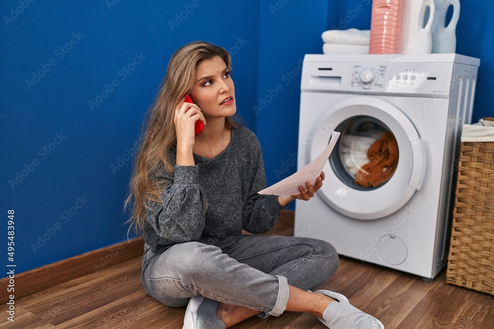 Young blonde woman talking on the smartphone waiting for washing machine at laundry room Young blonde woman talking on the smartphone waiting for washing machine at laundry room