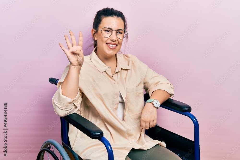 Young hispanic woman sitting on wheelchair showing and pointing up with fingers number four while smiling confident and happy. Young hispanic woman sitting on wheelchair showing and pointing up with fingers number four while smiling confident and happy.
