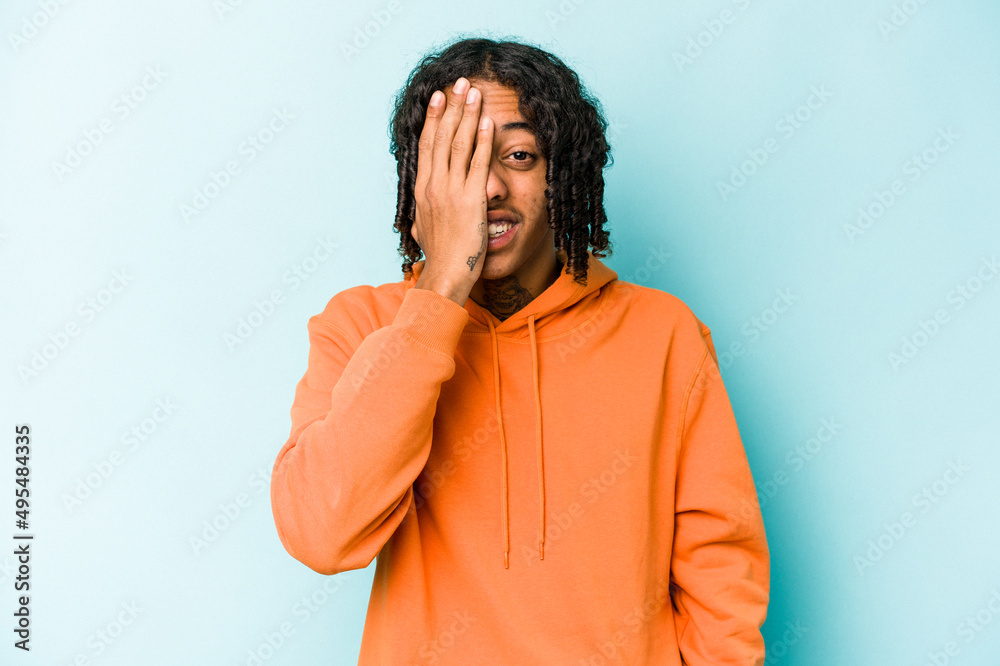 Young African American man isolated on blue background having fun covering half of face with palm. Young African American man isolated on blue background having fun covering half of face with palm.