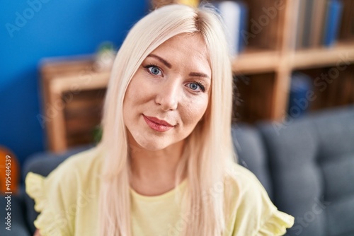 Young blonde woman smiling confident sitting on sofa at home