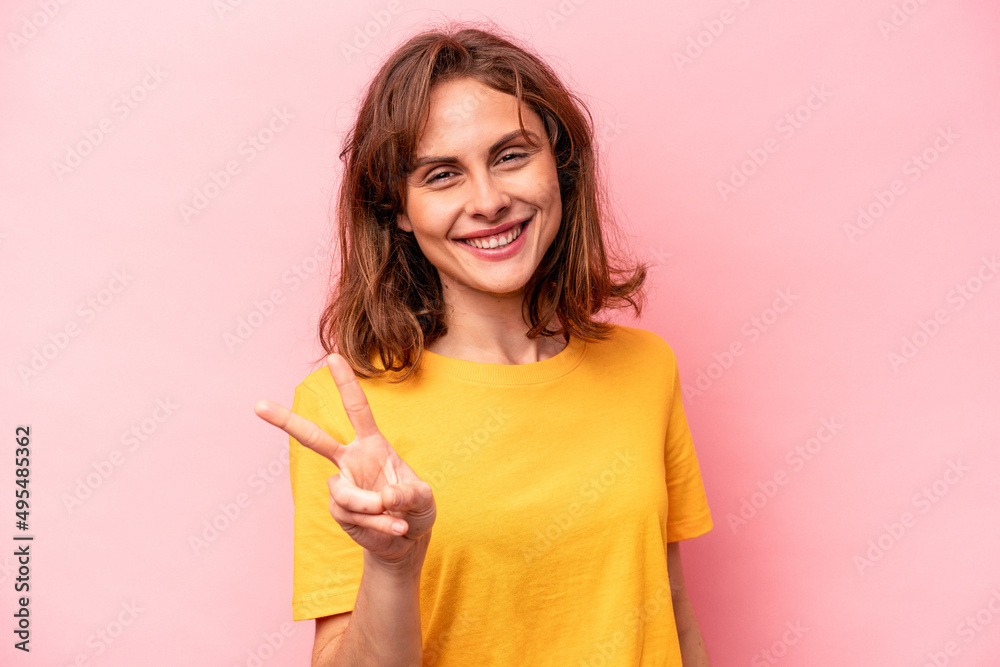 Young caucasian woman isolated on pink background showing victory sign and smiling broadly. Young caucasian woman isolated on pink background showing victory sign and smiling broadly.