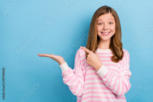 Obraz na plátně Photo of cheerful adorable girl indicate finger arm palm hold empty space isolat