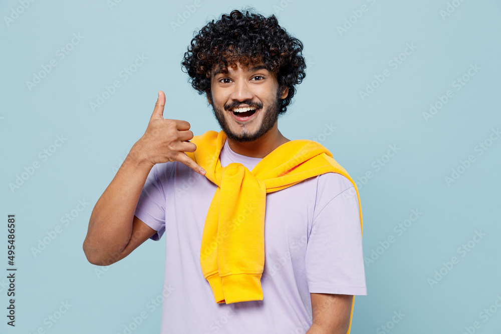 Excited joyful jubilant exultant young bearded Indian man 20s years old wears white t-shirt doing phone gesture like says call me back isolated on plain pastel light blue background studio portrait. Excited joyful jubilant exultant young bearded Indian man 20s years old wears white t-shirt doing phone gesture like says call me back isolated on plain pastel light blue background studio portrait.