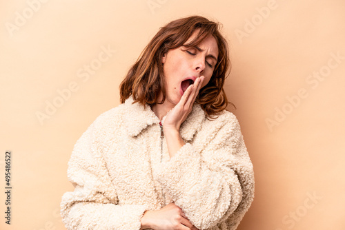 Young caucasian woman isolated on beige background yawning showing a tired gesture covering mouth with hand.