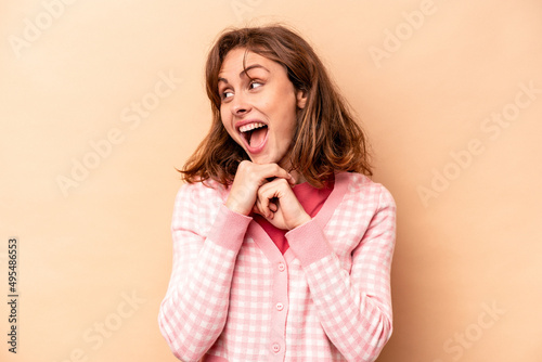 Young caucasian woman isolated on beige background praying for luck, amazed and opening mouth looking to front.