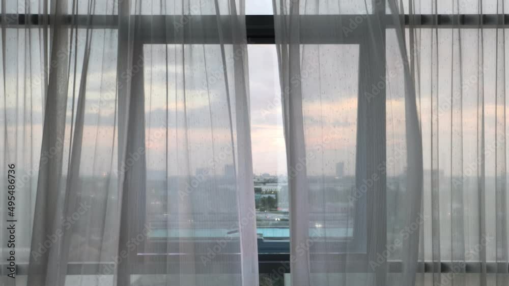 Curtains flutter in the wind from an open window in a wall of square windows