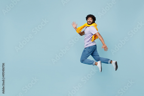 Full size body length side profile view cheerful fun happy young bearded Indian man 20s years old wear white t-shirt strolling pace walk isolated on plain pastel light blue background studio portrait