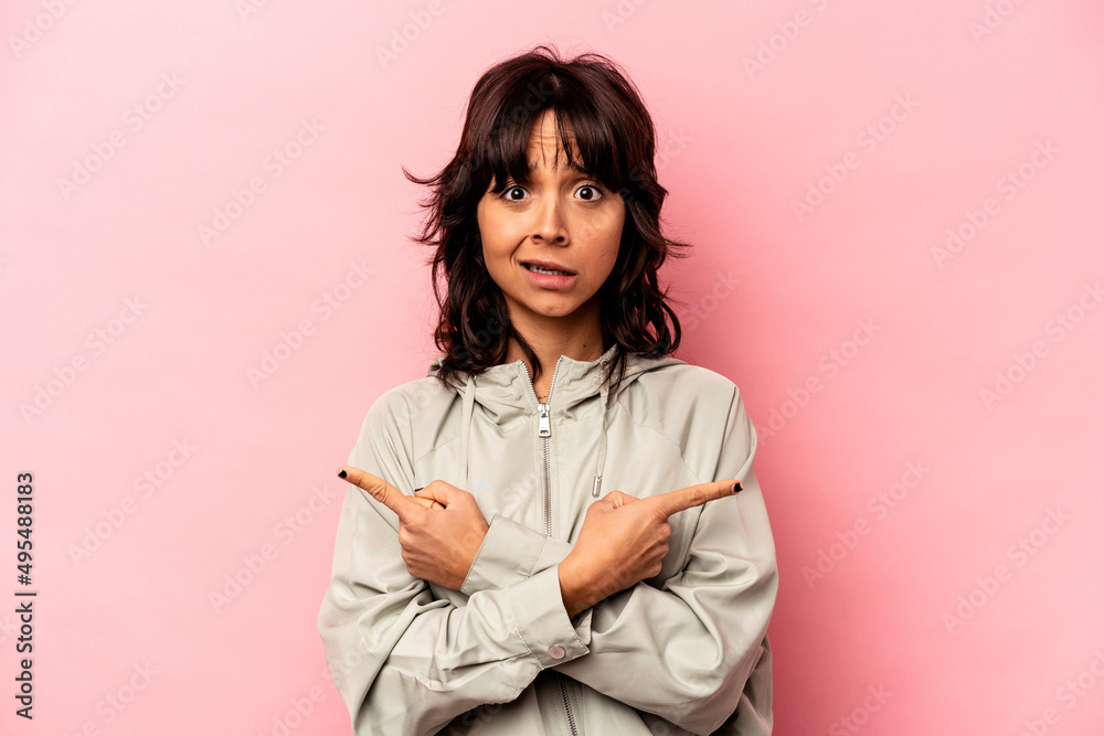 Young hispanic woman isolated on pink background points sideways, is trying to choose between two options. Young hispanic woman isolated on pink background points sideways, is trying to choose between two options.