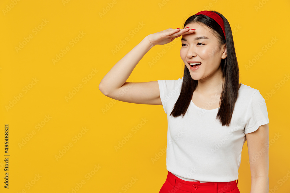 Young girl woman of Asian ethnicity 20s years old in white t-shirt hold hand at forehead look far away distance isolated on plain yellow background studio portrait. People emotions lifestyle concept Young girl woman of Asian ethnicity 20s years old in white t-shirt hold hand at forehead look far away distance isolated on plain yellow background studio portrait. People emotions lifestyle concept