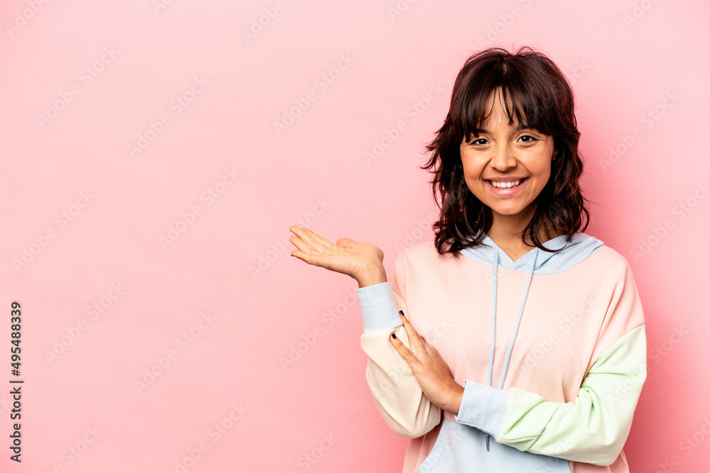 Young hispanic woman isolated on pink background showing a copy space on a palm and holding another hand on waist. Young hispanic woman isolated on pink background showing a copy space on a palm and holding another hand on waist.