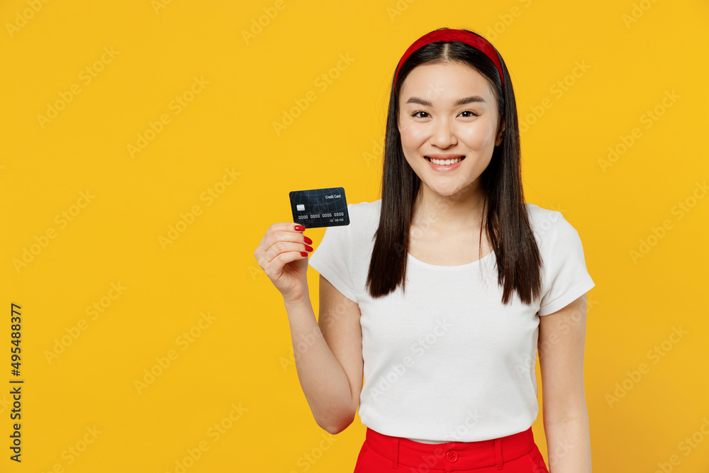 Happy excited young girl woman of Asian ethnicity 20s years old wear white t-shirt hold in hand credit bank card isolated on plain yellow background studio portrait. Achievement career wealth concept Happy excited young girl woman of Asian ethnicity 20s years old wear white t-shirt hold in hand credit bank card isolated on plain yellow background studio portrait. Achievement career wealth concept