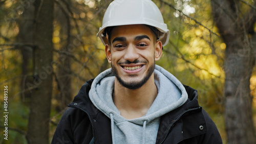 Male portrait young smiling hispanic professional worker in safety helmet posing outdoors looking at camera happy confident man forestry engineer stands in wood nature protection concept reforestation
