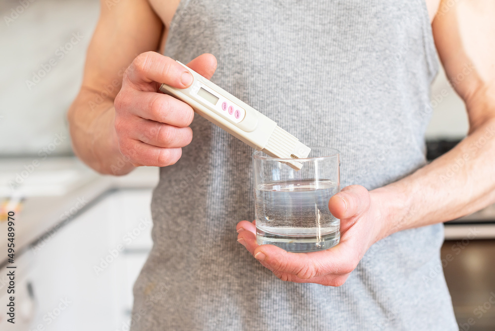 Checking the purity of water at home. Male hands and Glass of water