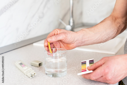 Checking the purity of water at home. Male hands and Glass of water, quality tester and universal litmus ph tester with color scale. Measuring the characteristics of drinking water.