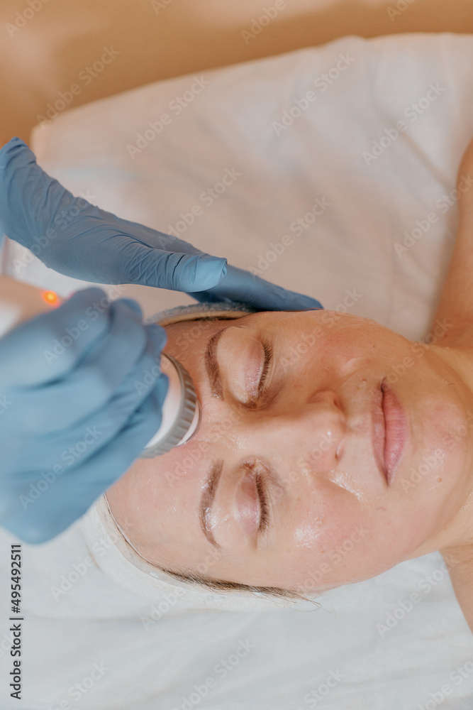the cosmetologist performs the procedure with a device with microcurrents for the face of a European woman and drives the device over the client's forehead. close-up the cosmetologist performs the procedure with a device with microcurrents for the face of a European woman and drives the device over the client's forehead. close-up