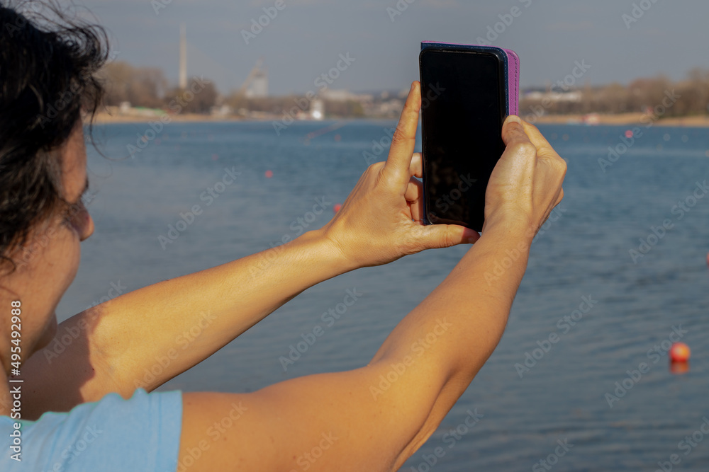 Middle aged woman taking a shot with her phone camera near a lake