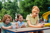 cheerful family using smartphones on playground in park.