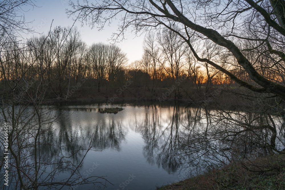 Lake with bare trees reflected in the water in the evening light.