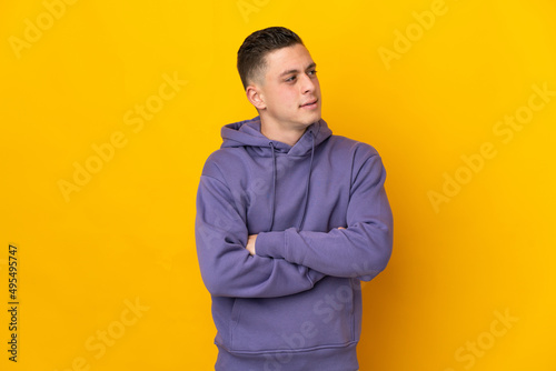 Young caucasian man isolated on yellow background looking to the side
