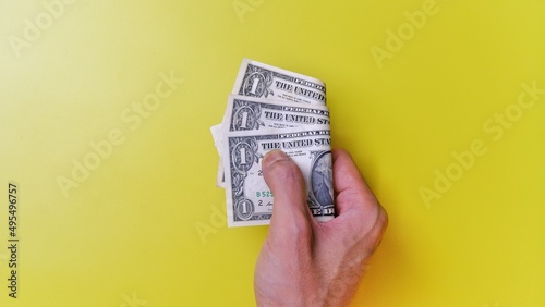 Man's hand is making a payment. Business Investment Economy Money Loan Saving Income Prosperity and Finance concept. Male hand showing dollar bills on yellow background. One Dollar. 1 US Dollar.