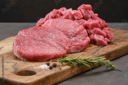 Fresh cut fillet of beef on a wooden board with salt, pepper, rosemary. Raw steak beef meat fillet ready to cook. Selective focus