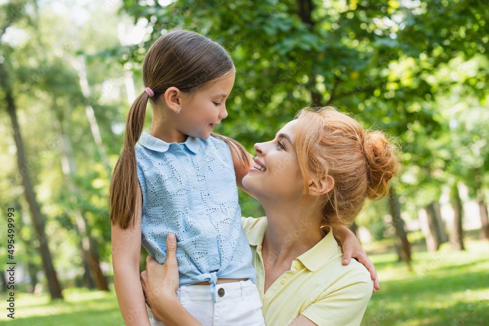 joyful woman and daughter embracing and looking at each other in summer park. joyful woman and daughter embracing and looking at each other in summer park.