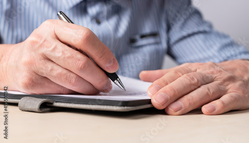 Man sitting at table and writing smth in notebook. Hands closeup. Education, scheduling concept. High quality photo