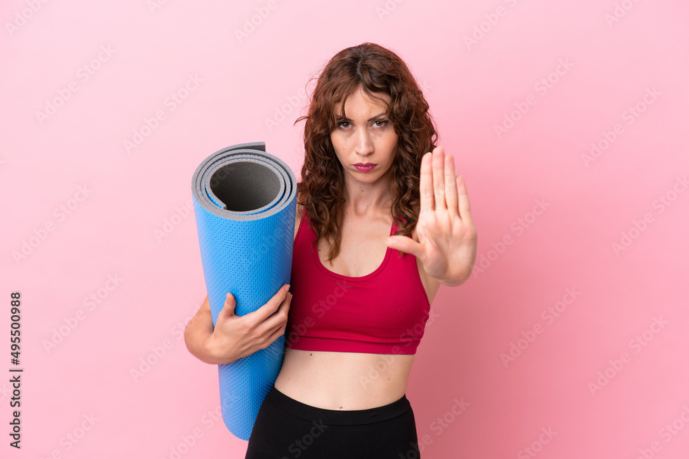 Young sport woman going to yoga classes while holding a mat isolated on pink background making stop gesture Young sport woman going to yoga classes while holding a mat isolated on pink background making stop gesture