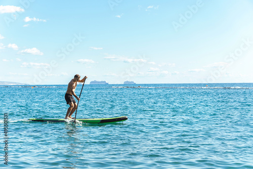 Young male surfer riding standup paddleboard in ocean. © blackday
