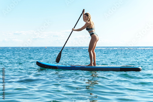 Young female surfer in bikini riding standup paddleboard in ocean. photo