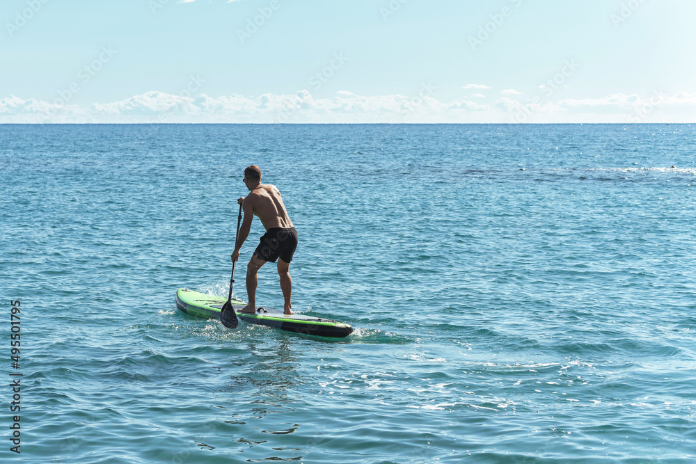 Young male surfer riding standup paddleboard in ocean.
