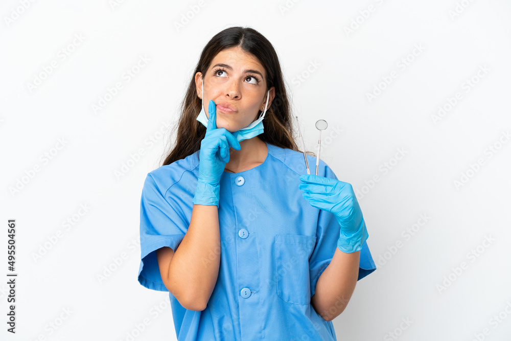Dentist woman holding tools over isolated white background having doubts while looking up Dentist woman holding tools over isolated white background having doubts while looking up