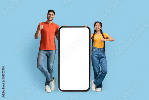 Cheerful Arab Couple Standing Near Big Blank Smartphone And Showing Thumb Up