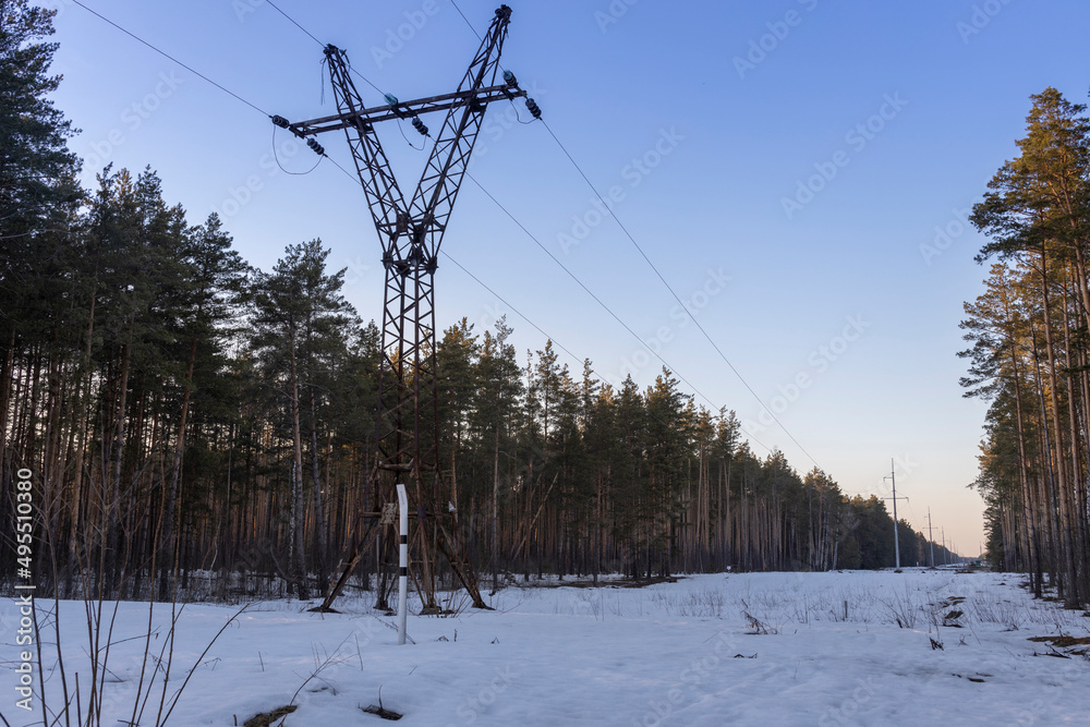 Winter landscape of power lines in a snowy field near the forest Winter landscape of power lines in a snowy field near the forest