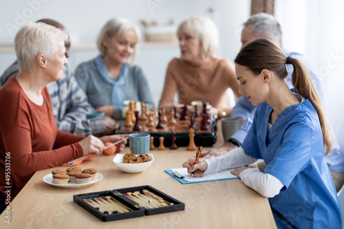 Female nurse sitting by multiracial group of pensioners, taking notes