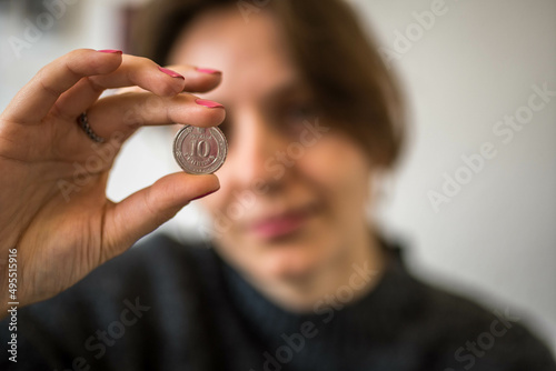 Silver 10 Ukrainian Hryvnia Coin with Cyrillic Alphabet Letters held in the Hand of a Woman Looking at it From the Background