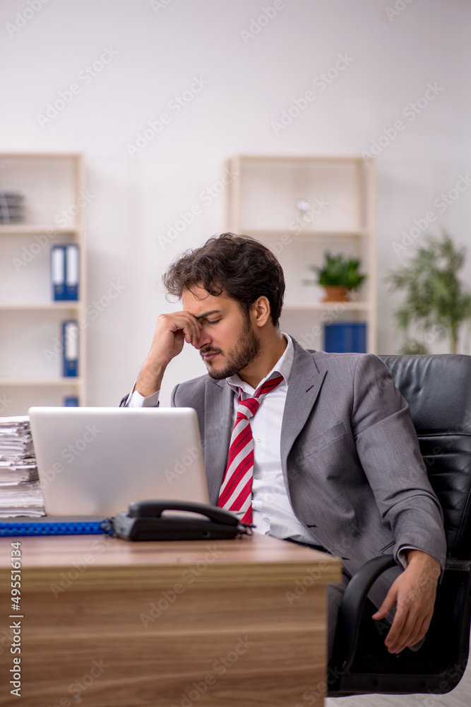 Young male employee unhappy with excessive work in the office Young male employee unhappy with excessive work in the office