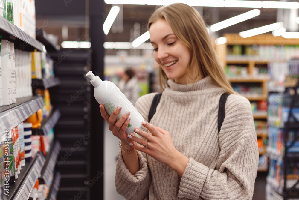Positive young blonde selecting bottle of shampoo in cosmetics department store
