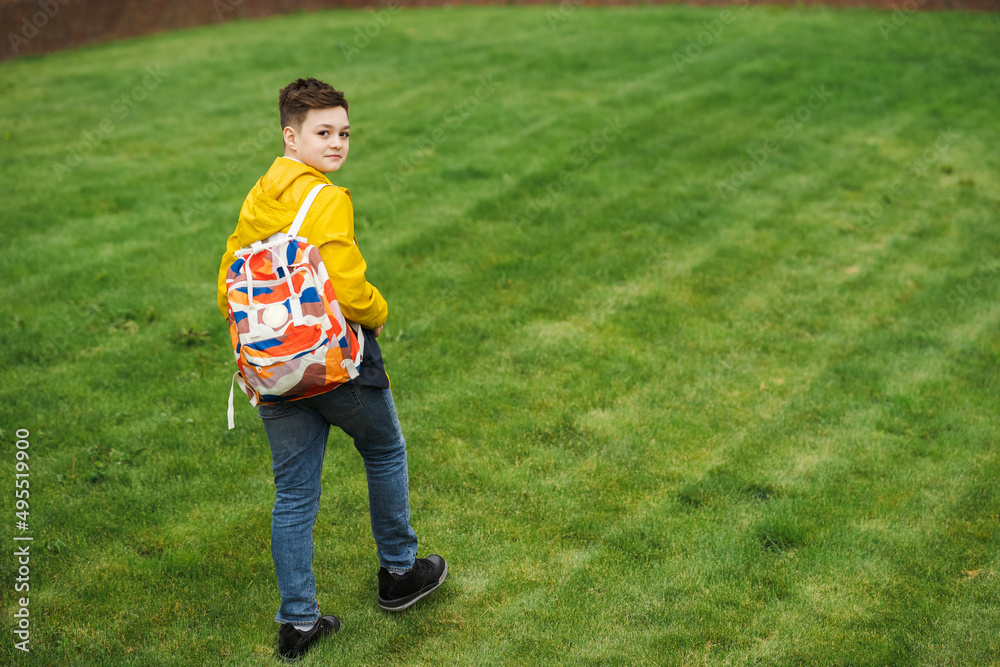 Handsome teenager with a backpack walks on a green lawn Handsome teenager with a backpack walks on a green lawn