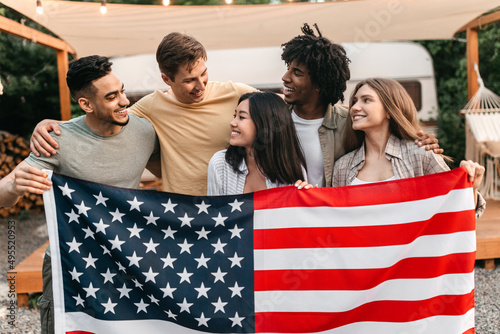Obraz na plátně Millennial interracial friends holding American flag and smiling in front of RV