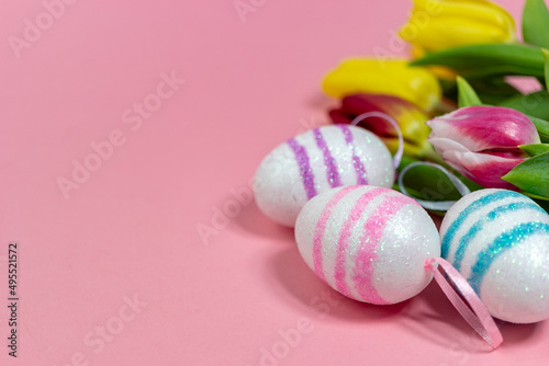 Easter border composition with Easter eggs and yellow and red tulips on a pink background. A stylish concept of minimalist decor. Space for copying. Festive flat banner with greeting card