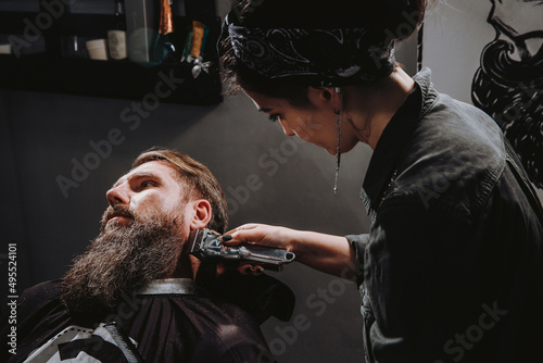 Women professional hairdresser serving client with thick big beard by clipper