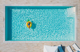 Sexy young female in swimsuit bikini, in a straw hat and sunglasses floating on blue swimming pool waves on giant inflatable Yellow Pineapple tube. Chill out summer vacation in luxury resorts concept.