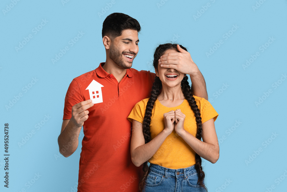 Fototapeta premium Loving Arab Man Holding Paper House Figure And Surprising His Excited Girlfriend