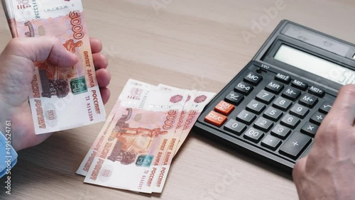 Men's hands count out five thousand Russian rubles and count on a calculator. Accounting, business accounting. Close-up.